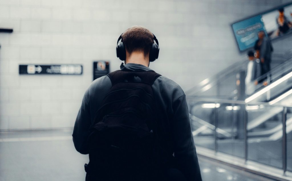 Back view of an adult man listening to music with headphones in a modern train station.