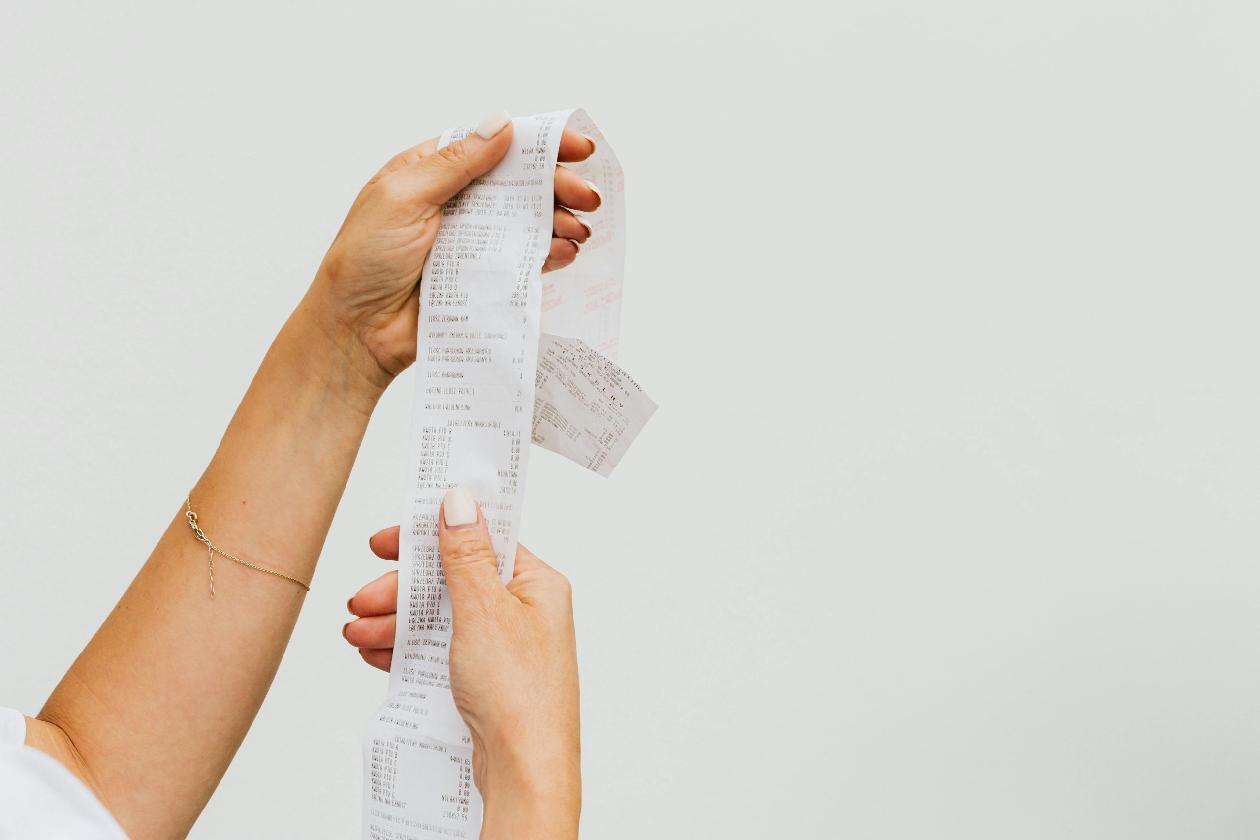 A detailed view of a person holding a long shopping receipt against a plain background.